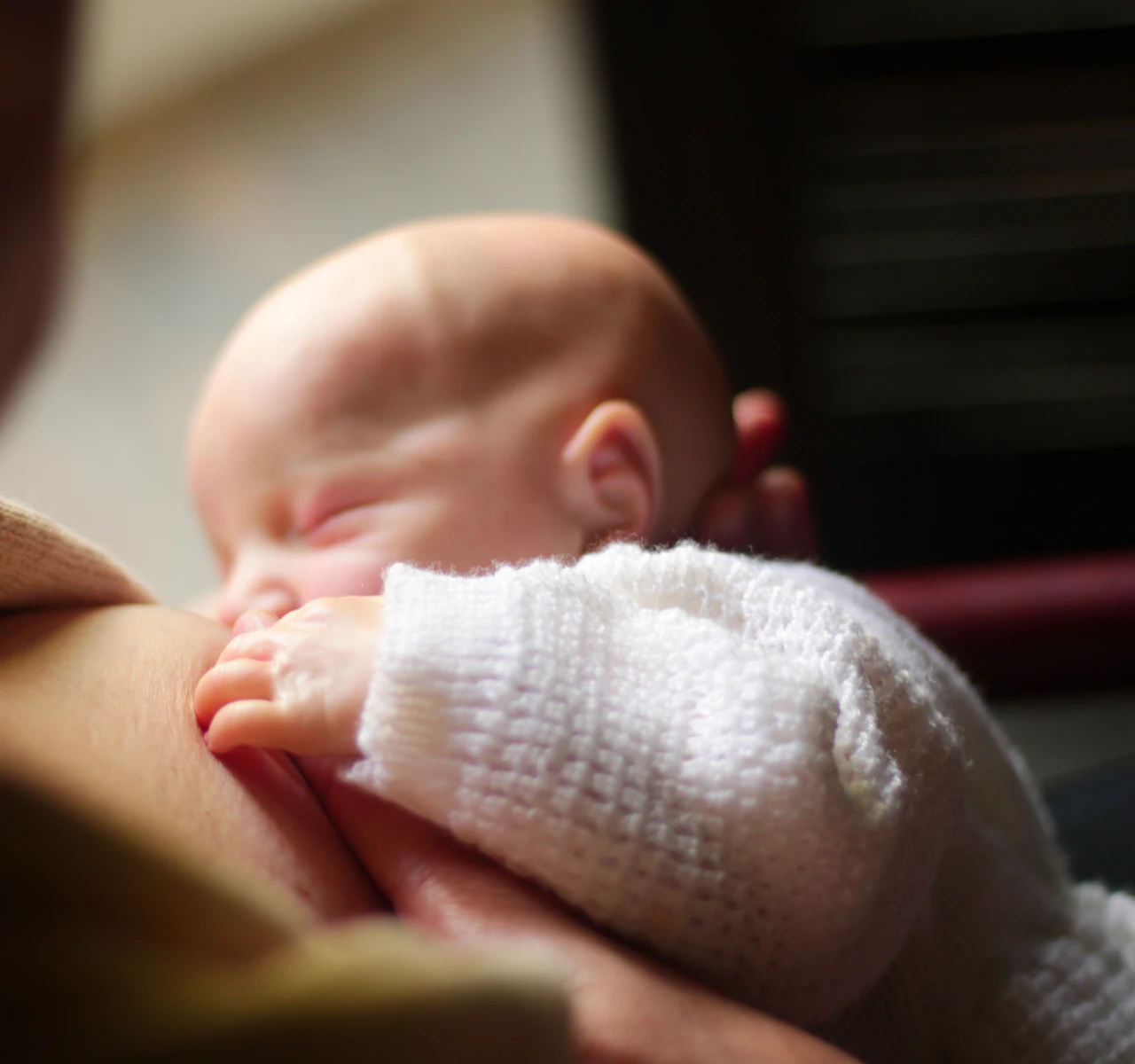 A newborn asleep in a mother’s arms in the soft light of a night feed